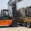 Forklift menurunkan mesin dari trailer di area pabrik Karawang
